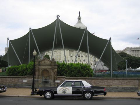 1991 Ford LTD Crown Victoria - black-and-white Highway Patrol sedan sits curbside in front of a large green tensile canopy near the Capitol.
