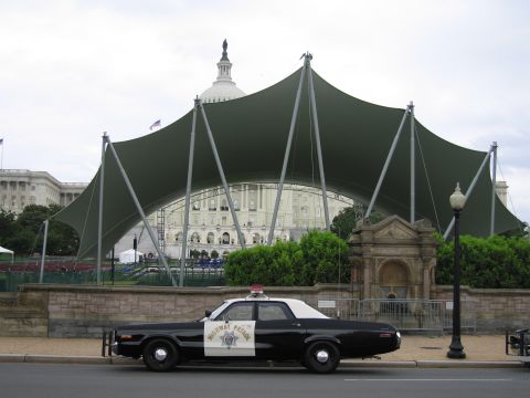 1991 Ford LTD Crown Victoria - black-and-white Highway Patrol sedan parks before a sweeping green canopy with the Capitol dome behind.
