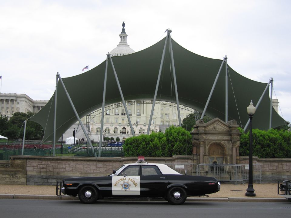 Black and white Highway Patrol sedan parked under a green canopy view