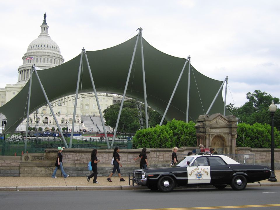 Pedestrians passing a black and white Highway Patrol sedan at the Capitol