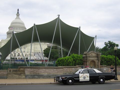 1991 Ford LTD Crown Victoria - black-and-white Highway Patrol sedan parks curbside as the Capitol dome rises behind a large green canopy.