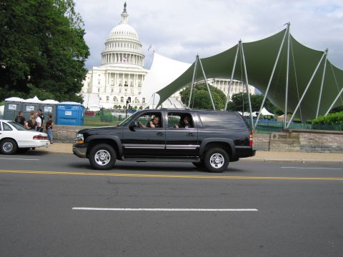 1991 Ford LTD Crown Victoria - black Chevrolet Suburban SUV drives along the street with the U.S. Capitol and a green canopy in the background.