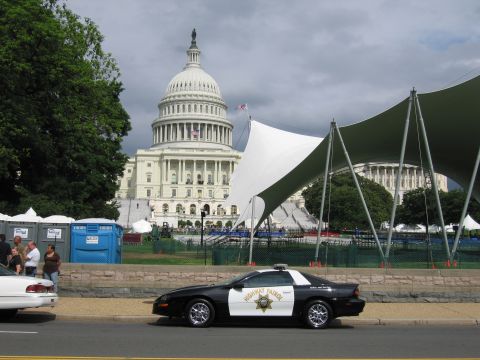1991 Ford LTD Crown Victoria - black-and-white Highway Patrol Chevrolet Camaro parks curbside with the U.S. Capitol rising behind.