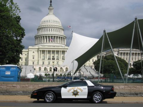 1991 Ford LTD Crown Victoria - black-and-white Highway Patrol Chevrolet Camaro parks curbside as the U.S. Capitol dome looms under cloudy sky.