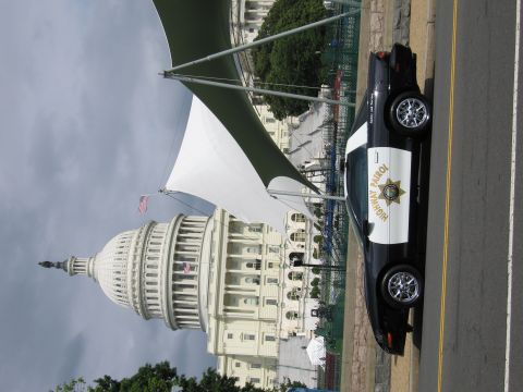 1991 Ford LTD Crown Victoria - black-and-white Highway Patrol cruiser parked on a road in front of a large white domed capitol-style building under a cloudy sky.