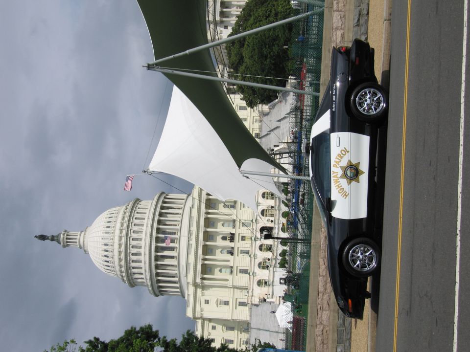 Black-and-white Highway Patrol police car parked on a street near a domed government building