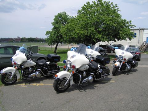 1991 Ford LTD Crown Victoria - Three white full-dress police touring motorcycles parked side by side on asphalt with a tree and buildings in the background.