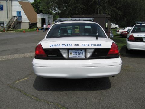 1991 Ford LTD Crown Victoria - Rear view of a white 'United States Park Police' sedan with a light bar, parked outdoors near a building and other cruisers.