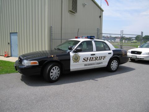 1991 Ford LTD Crown Victoria - black-and-white Frederick County Sheriff sedan with a star emblem and light bar parked beside a metal building.