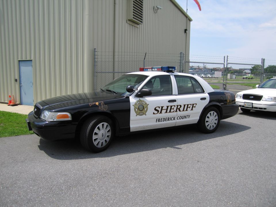 Black-and-white Frederick County Sheriff cruiser parked beside a metal building