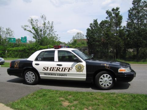 1991 Ford LTD Crown Victoria - Profile view of a black-and-white Frederick County Sheriff cruiser, unit 935, parked on grass near trees and highway signs.