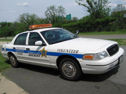 1991 Ford LTD Crown Victoria - white Frederick County Sheriff 'Community Assistance Patrol Volunteer' sedan with a blue stripe and amber light bar parked near trees.