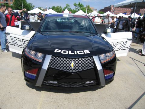 1991 Ford LTD Crown Victoria - Front view of a black-and-silver futuristic concept police car with a large mesh grille on display at a crowded outdoor event.