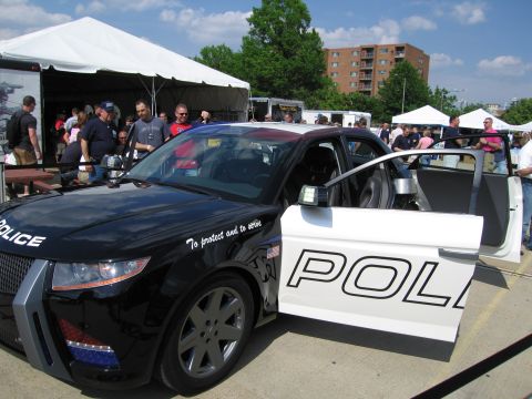 1991 Ford LTD Crown Victoria - black-and-white futuristic concept police car with 'To protect and to serve' lettering and doors open at an outdoor event.