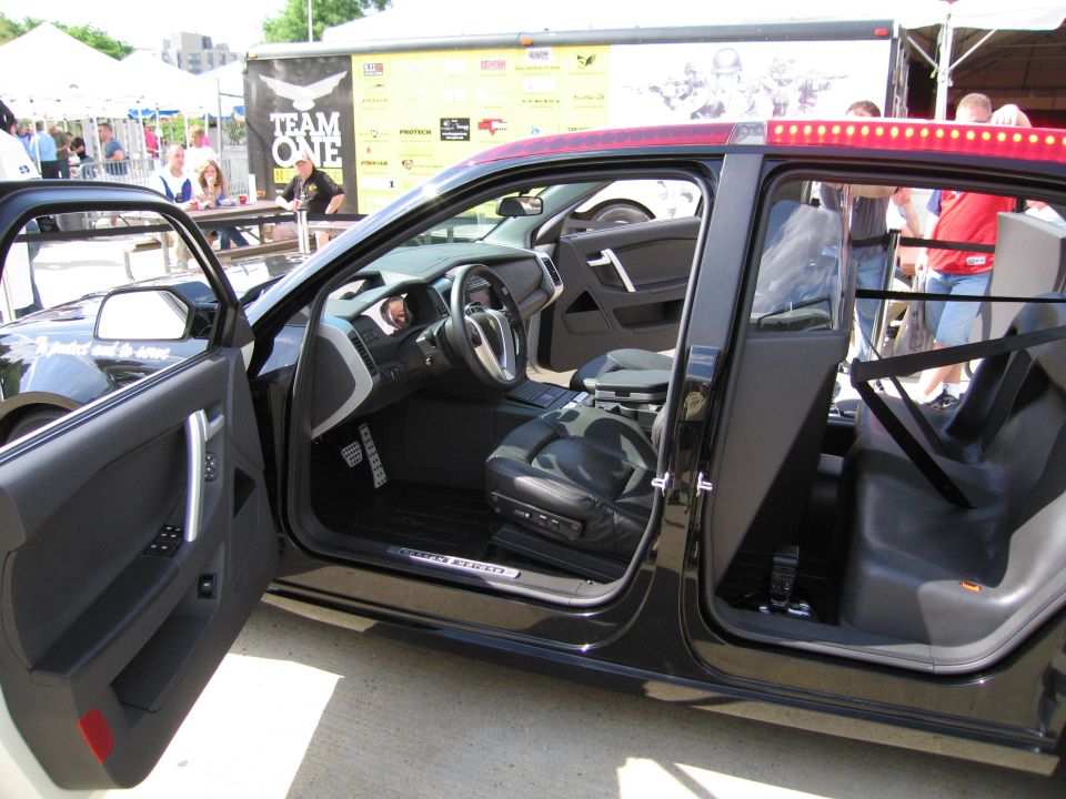 Open-door view of a black police vehicle interior at an outdoor event