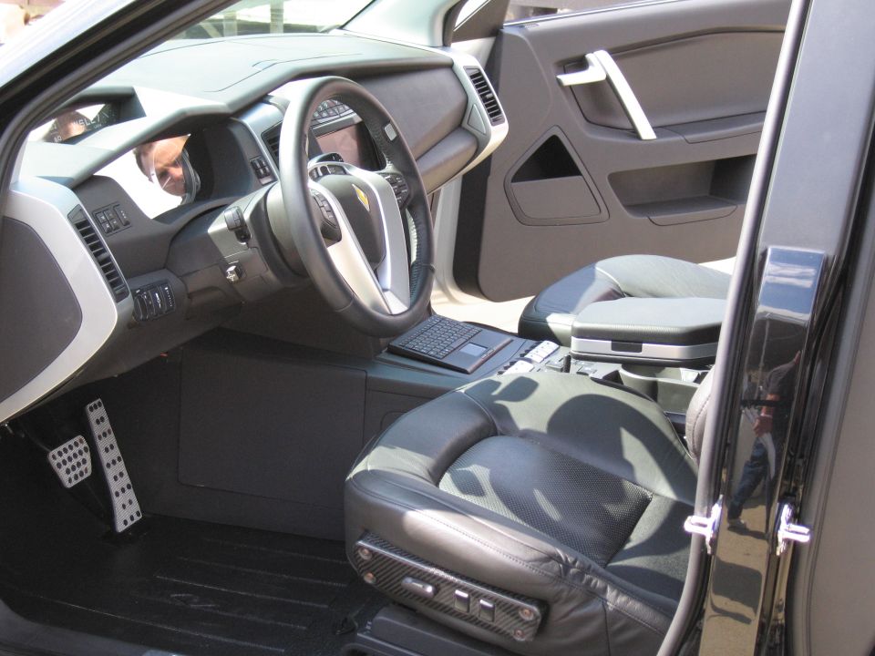 Interior of a vehicle showing steering wheel, console laptop, and camouflage seats