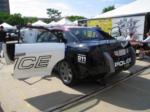 1991 Ford LTD Crown Victoria - Rear three-quarter view of a black-and-white police concept car marked POLICE and 911, mounted on a display ramp with a wing.