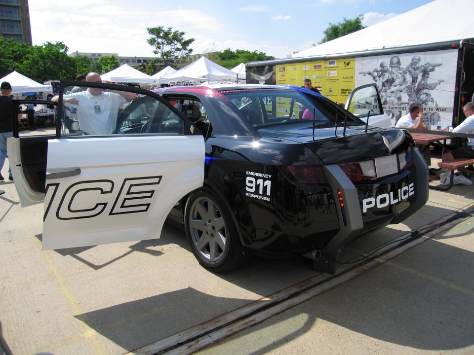 Rear three-quarter view of a black and white POLICE concept car with rear wing on a display ramp
