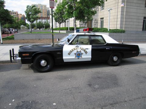 1991 Ford LTD Crown Victoria - black-and-white sedan lettered Highway Patrol with a star emblem and dome light sits curbside on a city street.