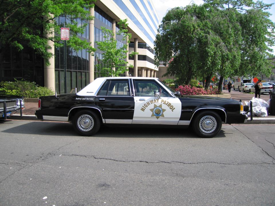 Black and white Highway Patrol four-door sedan parked along a tree-lined street