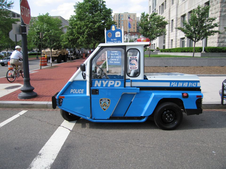Blue and white NYPD three-wheeled police scooter cart parked by a stop sign