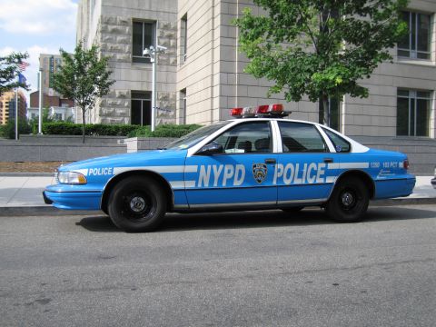 1991 Ford LTD Crown Victoria - two-tone blue NYPD police sedan lettered POLICE with a roof light bar is parked along a curb by a building.