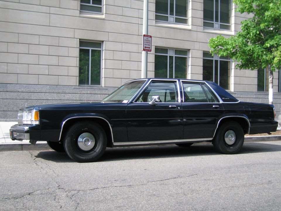 Dark blue full-size sedan parked at the curb in front of a stone building