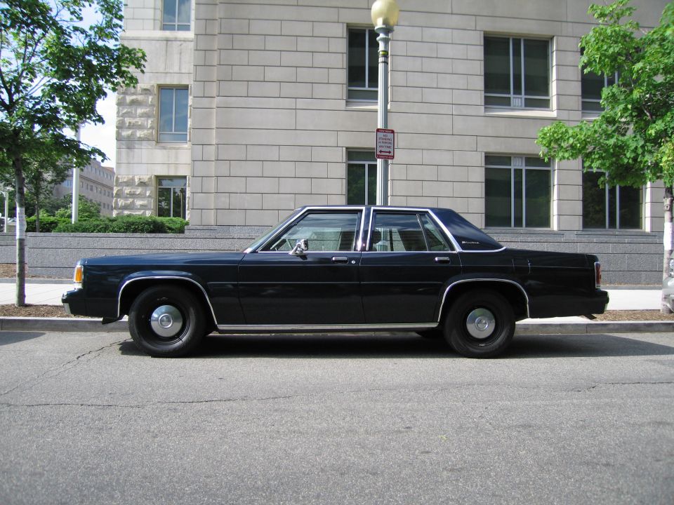 Side profile of a dark blue full-size sedan parked by a lamppost and building