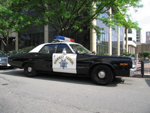 1991 Ford LTD Crown Victoria - black-and-white Highway Patrol four-door sedan with a star emblem and roof lights sits parked on a downtown street.