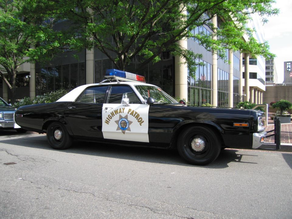 Black and white Highway Patrol 1970s sedan parked on a city street