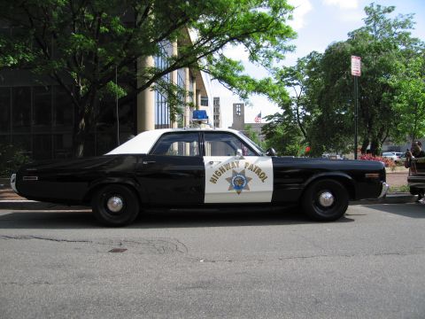 1991 Ford LTD Crown Victoria - Side profile of a black-and-white Highway Patrol four-door sedan with a blue dome light parked along a curb.