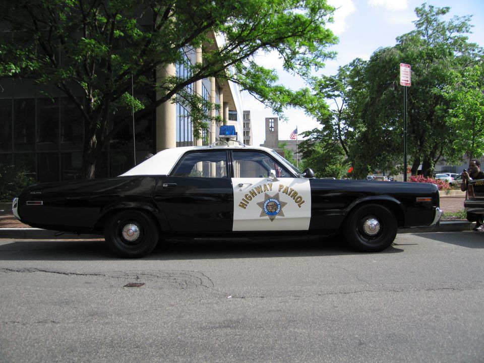 Black and white Highway Patrol sedan in side profile on a city street