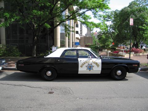 1991 Ford LTD Crown Victoria - black-and-white Highway Patrol four-door sedan with a star emblem sits parked along a tree-shaded city curb.