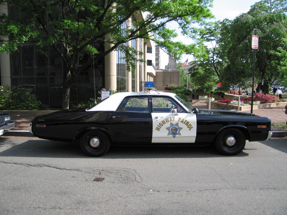 Black and white Highway Patrol sedan parked along a tree-lined curb