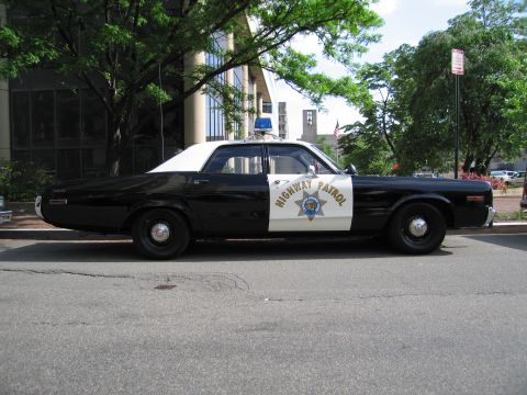 1991 Ford LTD Crown Victoria - Side view of a black-and-white Highway Patrol four-door sedan with a blue light parked on a downtown street.