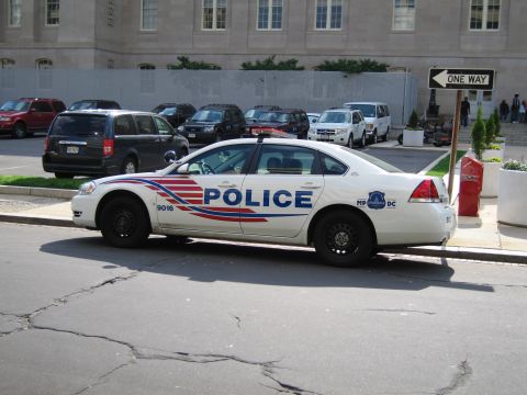 1991 Ford LTD Crown Victoria - white Metropolitan Police sedan lettered POLICE with red-and-blue striping sits parked near a one-way sign and lot.