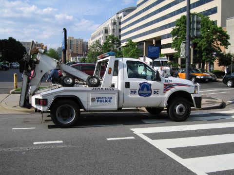 1991 Ford LTD Crown Victoria - white Metropolitan Police flatbed tow truck with a raised boom and Jerr-Dan lettering sits at a downtown crosswalk.