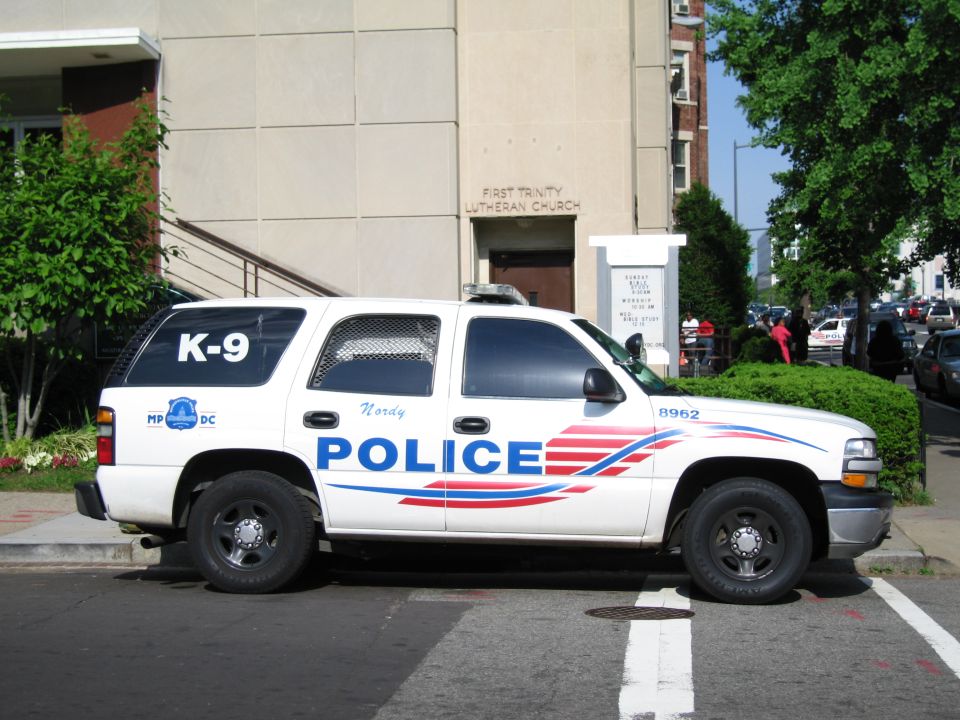 White Police K-9 SUV with red and blue stripe parked by a church