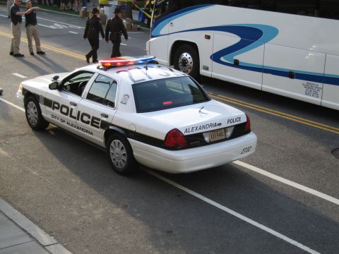 1991 Ford LTD Crown Victoria - black-and-white City of Alexandria Police sedan with a light bar is parked beside a tour bus as officers walk nearby.