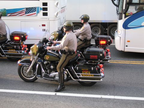 1991 Ford LTD Crown Victoria - Two Maryland State Trooper officers in tan uniforms ride black Harley-Davidson police motorcycles on a street between buses.