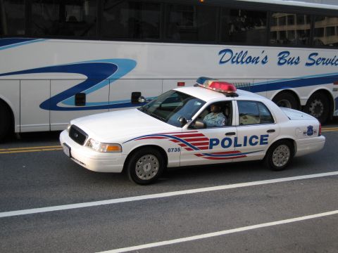1991 Ford LTD Crown Victoria - white Metropolitan Police sedan lettered POLICE with an officer inside is parked next to a Dillon's Bus Service coach.