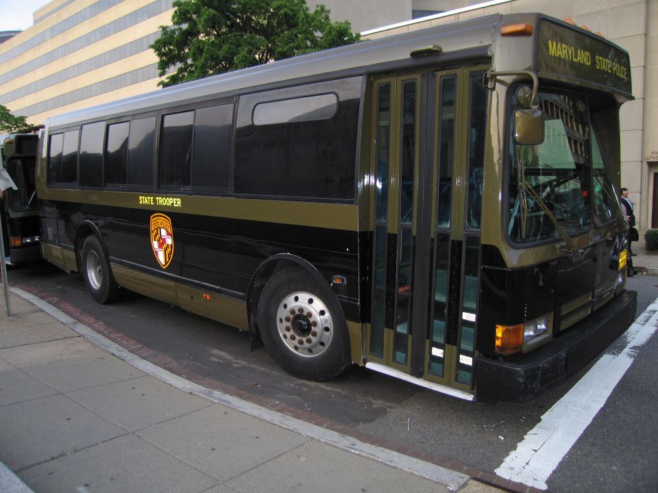 Black and gold Maryland State Police bus parked on a city street curb