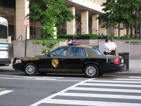 1991 Ford LTD Crown Victoria - Side view of a black and tan Maryland State Trooper sedan parked at a crosswalk with people on the sidewalk behind.