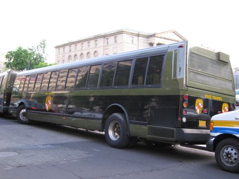 1991 Ford LTD Crown Victoria - Rear three-quarter view of an olive and black Maryland State Trooper bus parked on a city street near other buses.