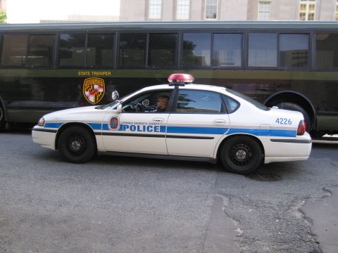1991 Ford LTD Crown Victoria - Side view of a white and blue Prince George's County Police Impala number 4226 next to an olive State Trooper bus.