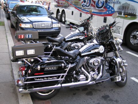 1991 Ford LTD Crown Victoria - Two black police Harley-Davidson motorcycles with windshields and saddlebags parked curbside near a sedan and a coach.