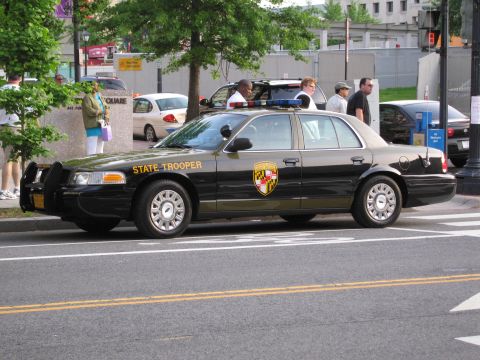 1991 Ford LTD Crown Victoria - black and tan Maryland State Trooper Ford sedan parked along a city street with pedestrians on the sidewalk.