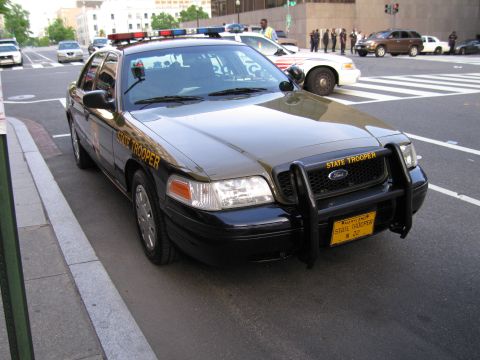 1991 Ford LTD Crown Victoria - black and tan Maryland State Trooper Ford sedan with a black push bumper parked at a downtown intersection.