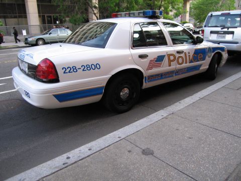 1991 Ford LTD Crown Victoria - white United States Capitol Police Ford sedan with flag graphics and a light bar parked along a city street.