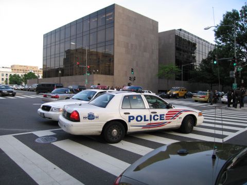 1991 Ford LTD Crown Victoria - white Metropolitan Police Ford sedan with a light bar at a city intersection in front of a dark stone building.